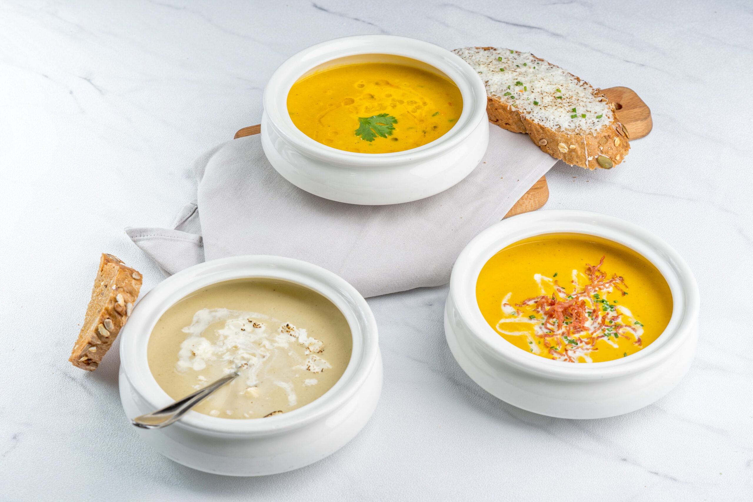 Top view of assorted creamy soups with artisan sliced bread, perfect for a warming meal.